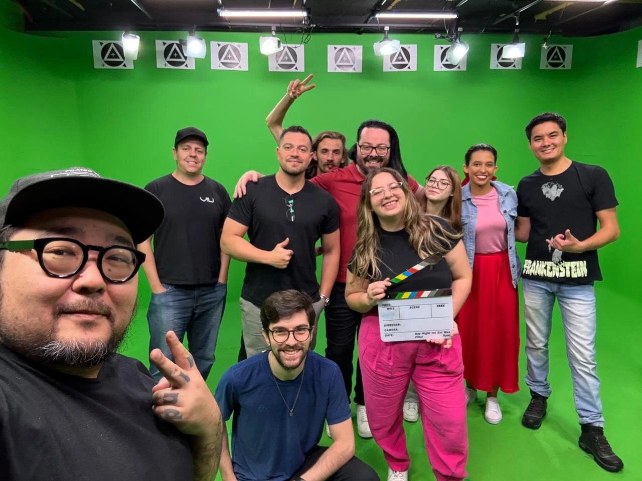 O time da LIFT Studios reunido dentro do estúdio de chroma, entre refletores e marcadores de tracking, um deles segurando a claquete.